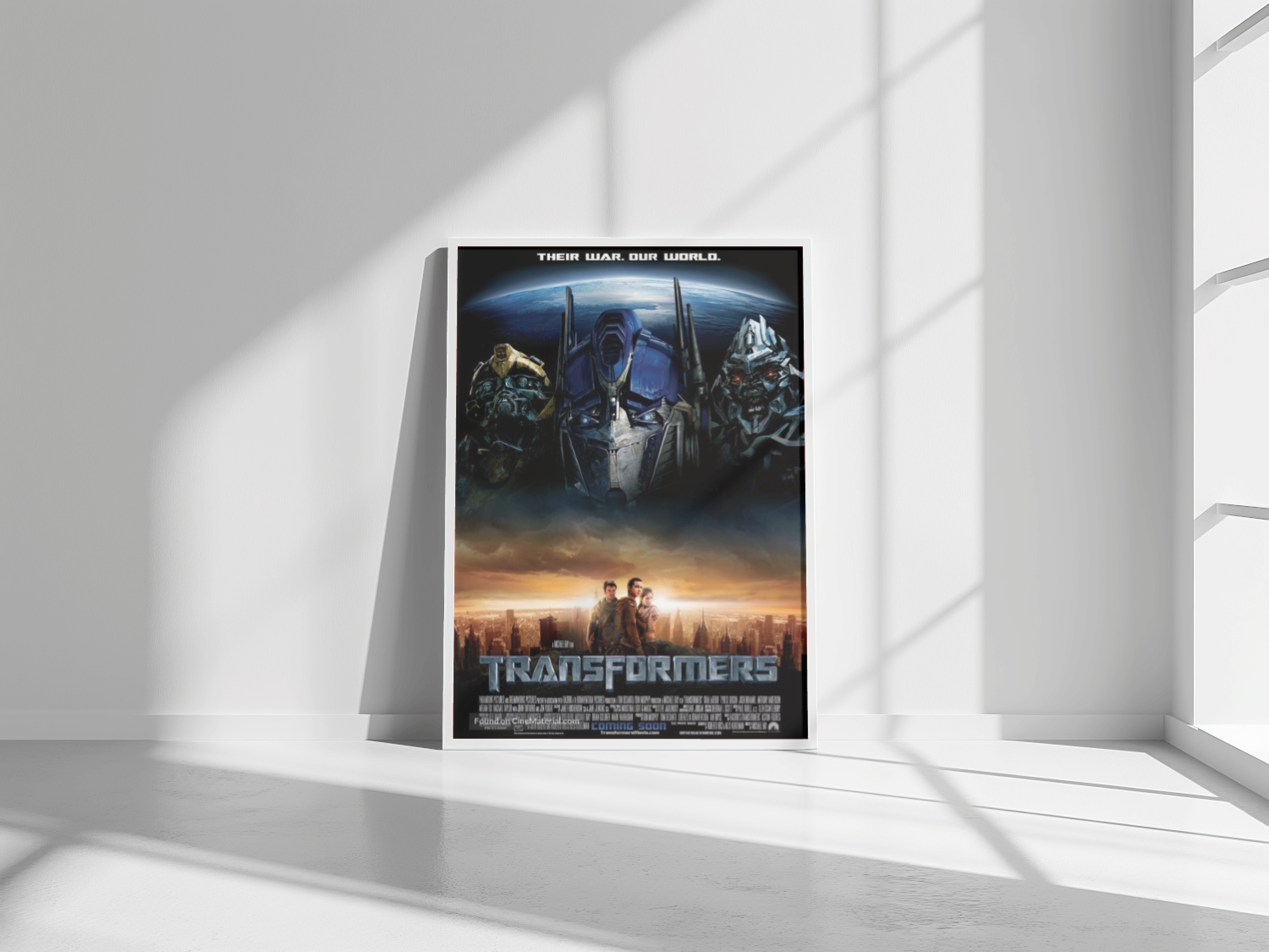 A framed movie poster leaning against a blank wall. The poster is for the movie Transformers