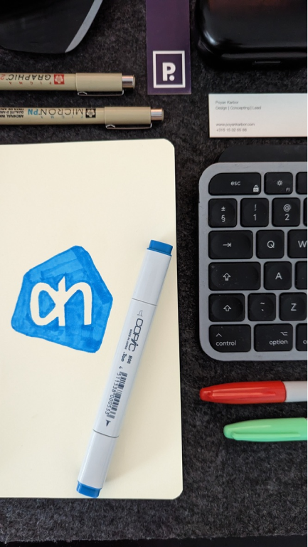 An image of a sketchbook with markers surrounding it. Albert Heijn's logo has been sketched on one of the pages.